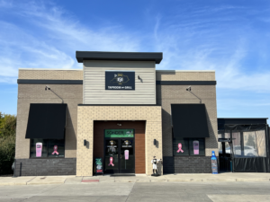 Front exterior of The 859 Taproom and Grill in Florence, Kentucky, with brick facade, black awnings, and pink ribbon decals displayed on the windows.