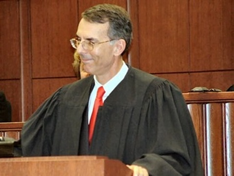 Judge Lewis Grant Paisley stands in a Kentucky courtroom wearing judicial robes and a red tie.