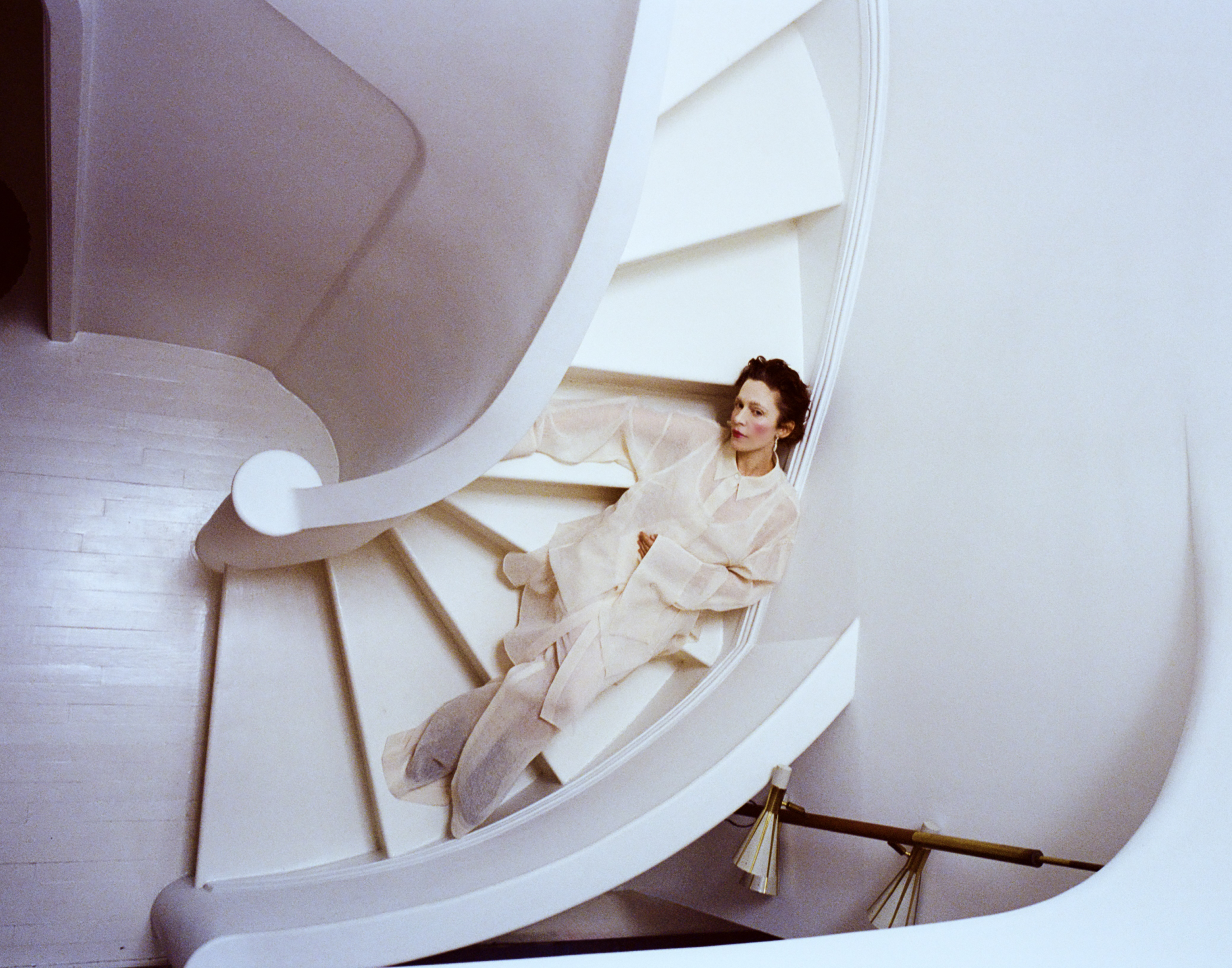 Actor and writer Jen Tullock smiles in a warmly lit portrait, wearing a dark jacket and gold hoop earrings. The Kentucky-born star of Severance and playwright of Nothing Can Take You From the Hand of God poses against a soft backdrop, reflecting her grounded, expressive personality and creative spirit.