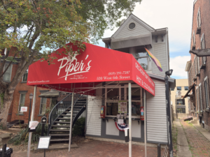 Exterior of Piper’s Ice Cream Bar in Covington, Kentucky, featuring a bright red awning, a walk-up service window, and a Progress Pride flag above the entrance.