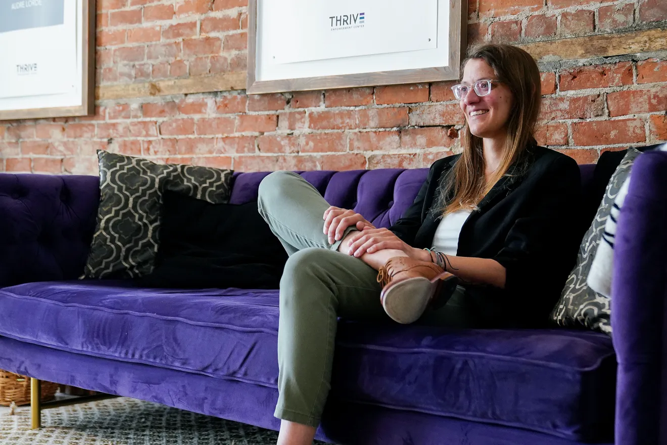 Emily Schubert, a licensed clinical social worker, sits on a purple couch inside Thrive Empowerment Center in Covington, Kentucky, a trauma-informed LGBTQ-affirming community space focused on safety, healing, and advocacy amid rising anti-LGBTQ+ violence in Northern Kentucky.
