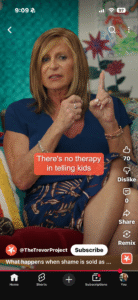 Screenshot of Dr. Bobbie Glass speaking in a video for The Trevor Project. She is seated on a couch wearing a navy blue dress, gesturing with one finger raised as she talks. On-screen text reads, “There’s no therapy in telling kids.” The YouTube Shorts interface is visible, showing the account @TheTrevorProject and engagement icons along the right side.