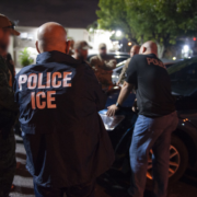 U.S. Immigration and Customs Enforcement officers and law enforcement agents gather around a vehicle during an immigration enforcement operation at night.