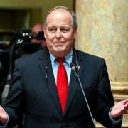 Kentucky Sen. Gex Williams speaks at a podium inside the Kentucky State Capitol in Frankfort while addressing lawmakers and media.