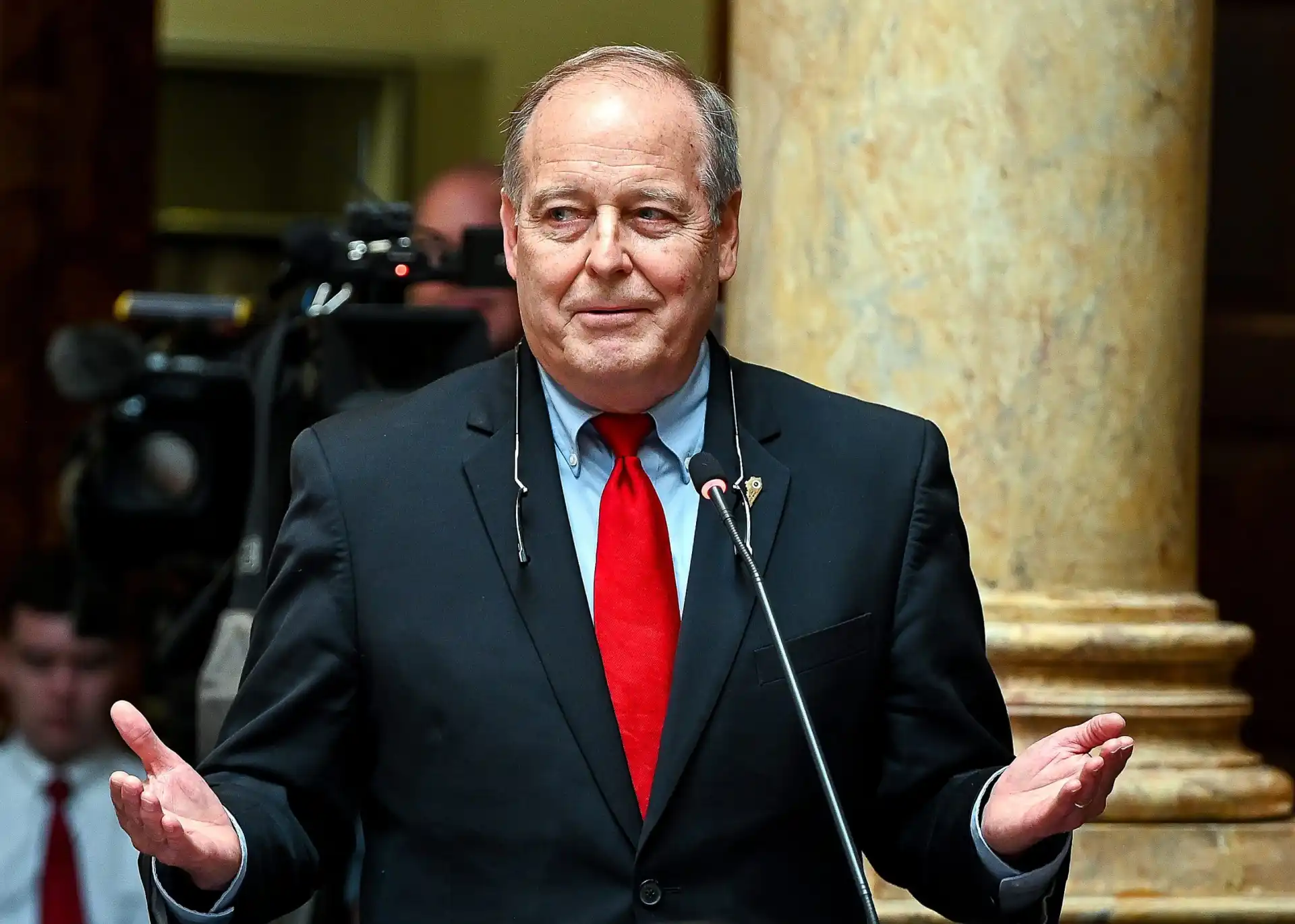 Kentucky Sen. Gex Williams speaks at a podium inside the Kentucky State Capitol in Frankfort while addressing lawmakers and media.