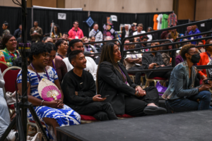 A diverse crowd of LGBTQ conference attendees seated in a large ballroom at a Creating Change conference, smiling and engaged with a presentation.