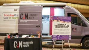 A CAN Community Health mobile health van parked inside a conference venue next to a Creating Change Health and Wellness Space sign.