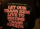 A person wearing a black Pride t-shirt reading "Let our trans kids live to become trans adults" at a community gathering in Kentucky