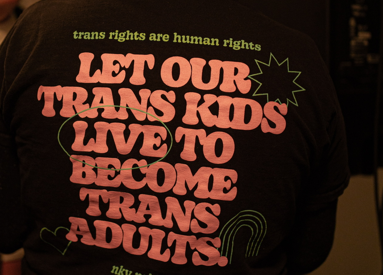 A person wearing a black Pride t-shirt reading "Let our trans kids live to become trans adults" at a community gathering in Kentucky